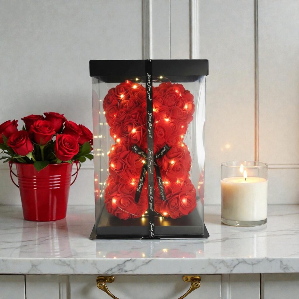 Czerwony miś wykonany z piankowych róż, ozdobiony światełkami LED, zamknięty w przezroczystym ozdobnym pudełku z czarną wstążką.
