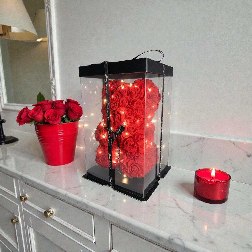 Czerwony miś wykonany z piankowych róż, ozdobiony światełkami LED, zamknięty w przezroczystym ozdobnym pudełku z czarną wstążką.